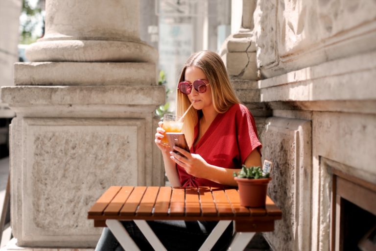 woman drinking while holding smartphone